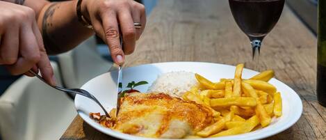 Un plato con pescado, arroz, papas fritas, una copa de vino tinto y una botella sobre una mesa de madera.