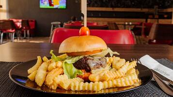 A meal consisting of a burger with a toothpick, fries, and a small tomato on a black plate, set on a table with a woven mat.