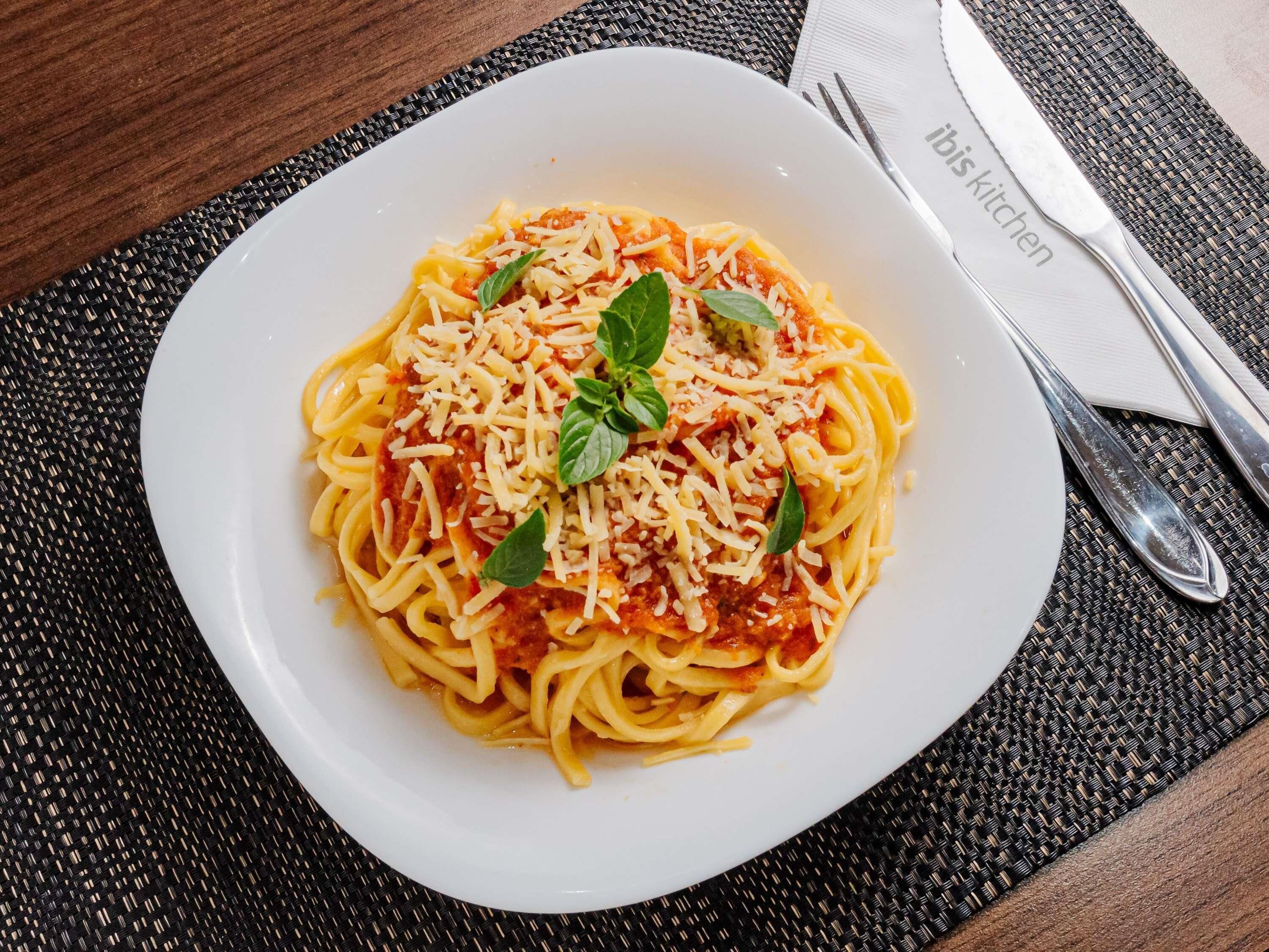 Une assiette de spaghettis à la sauce tomate et au fromage, garnie de feuilles de basilic, sur une assiette blanche.
