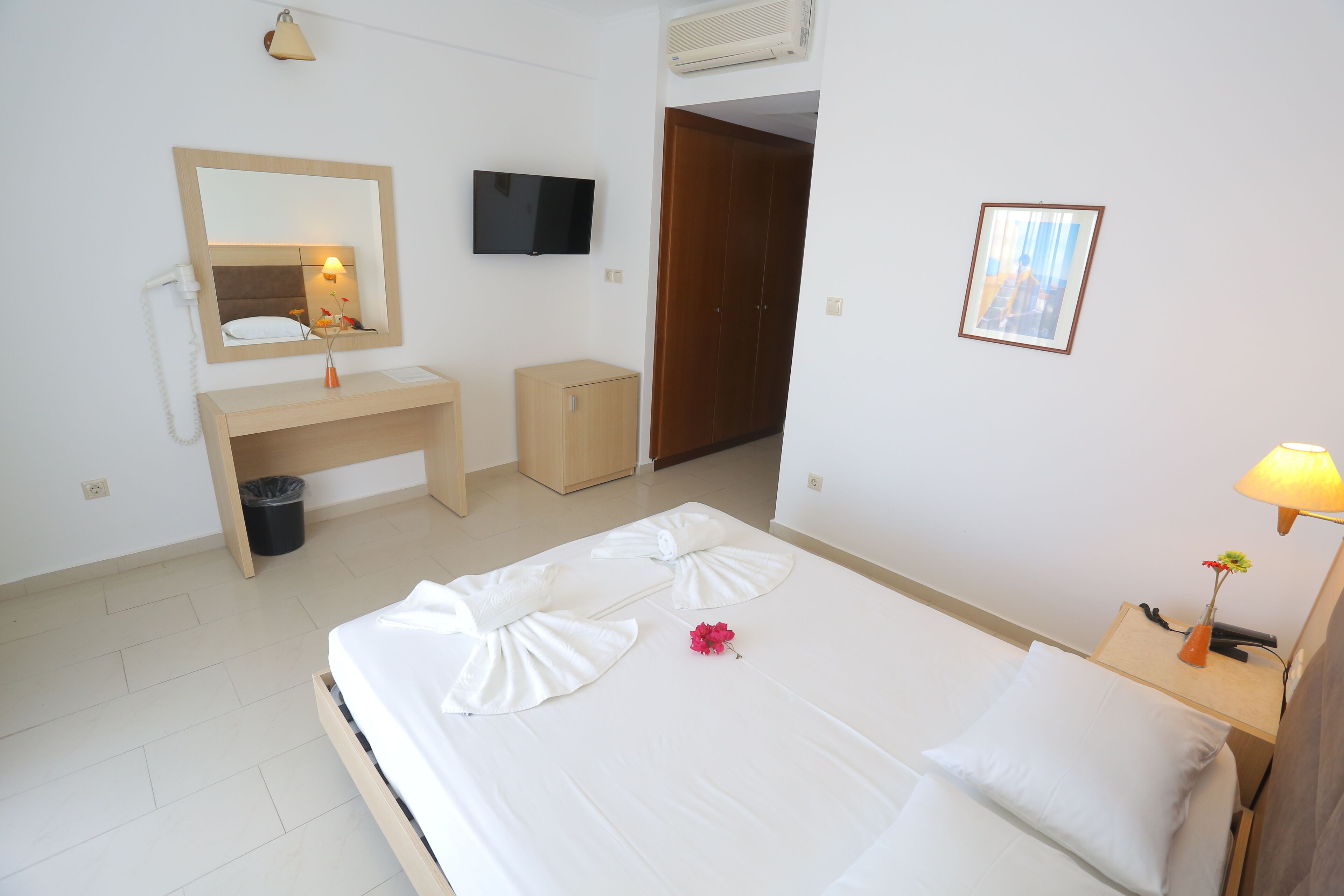 A hotel room with a bed, bedside table, lamp, mirror, wardrobe, and a TV.