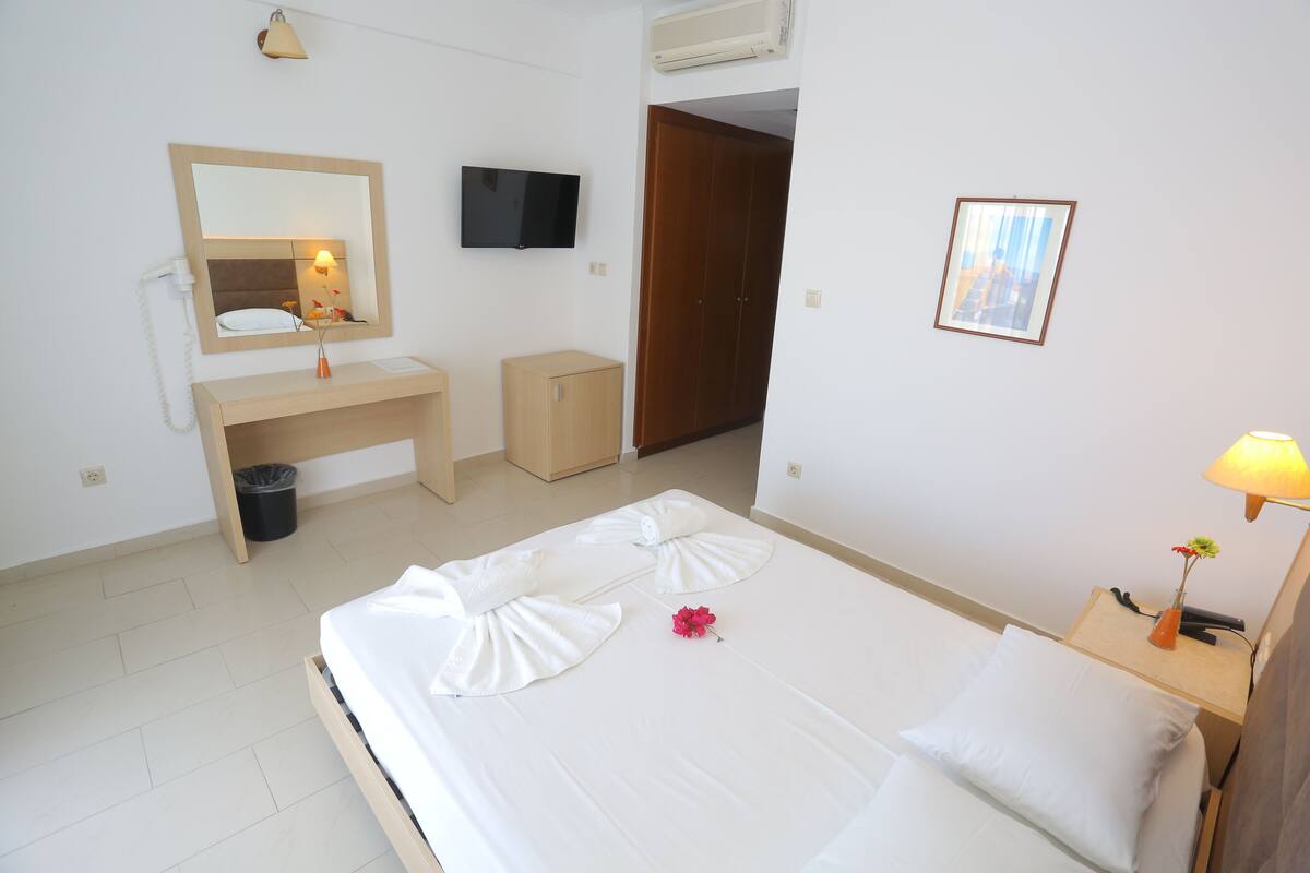A hotel room with a bed, bedside table, lamp, mirror, wardrobe, and a TV.