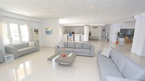 A modern living room with a grey sofa, a coffee table, and a kitchen area in the background. - Hilltop Hotel (Kassandra)