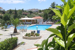 A pool area with lounge chairs, a palm tree, and a building with a red roof.