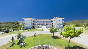 A multi-story building with a central entrance, surrounded by a well-maintained garden with various plants and a paved driveway. - Hilltop Hotel (Kassandra)