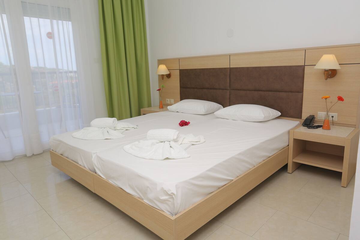 Una cama bien hecha con sábanas blancas, dos mesitas de noche con lámparas y una cortina verde.