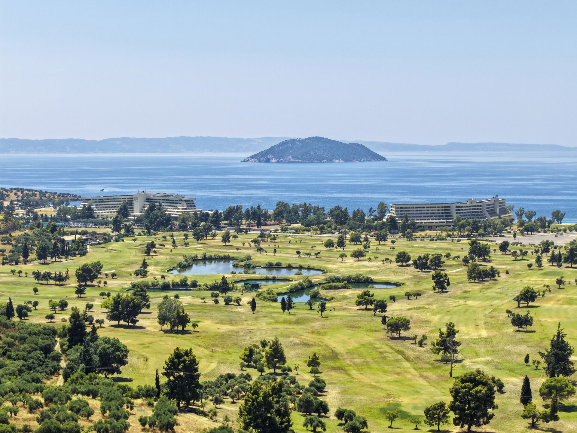 A coastal landscape with a golf course, a body of water, and buildings in the distance.