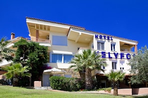Een hotel met een gebouw van twee verdiepingen, balkons en een tuin met palmbomen en struiken.