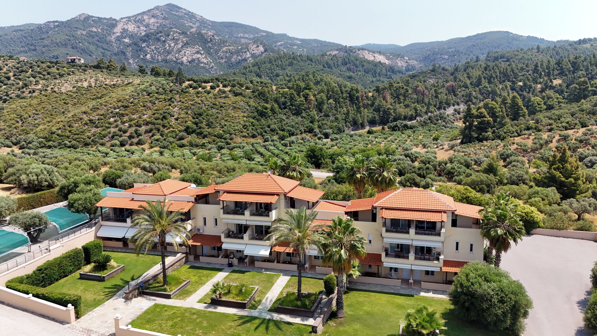 A multi-story hotel with a Mediterranean architectural style, featuring terracotta roofs and a landscaped courtyard with palm trees.