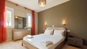 Une chambre d’hôtel avec un grand lit, des tables de chevet, une commode, un miroir et des lampes fixées au mur.