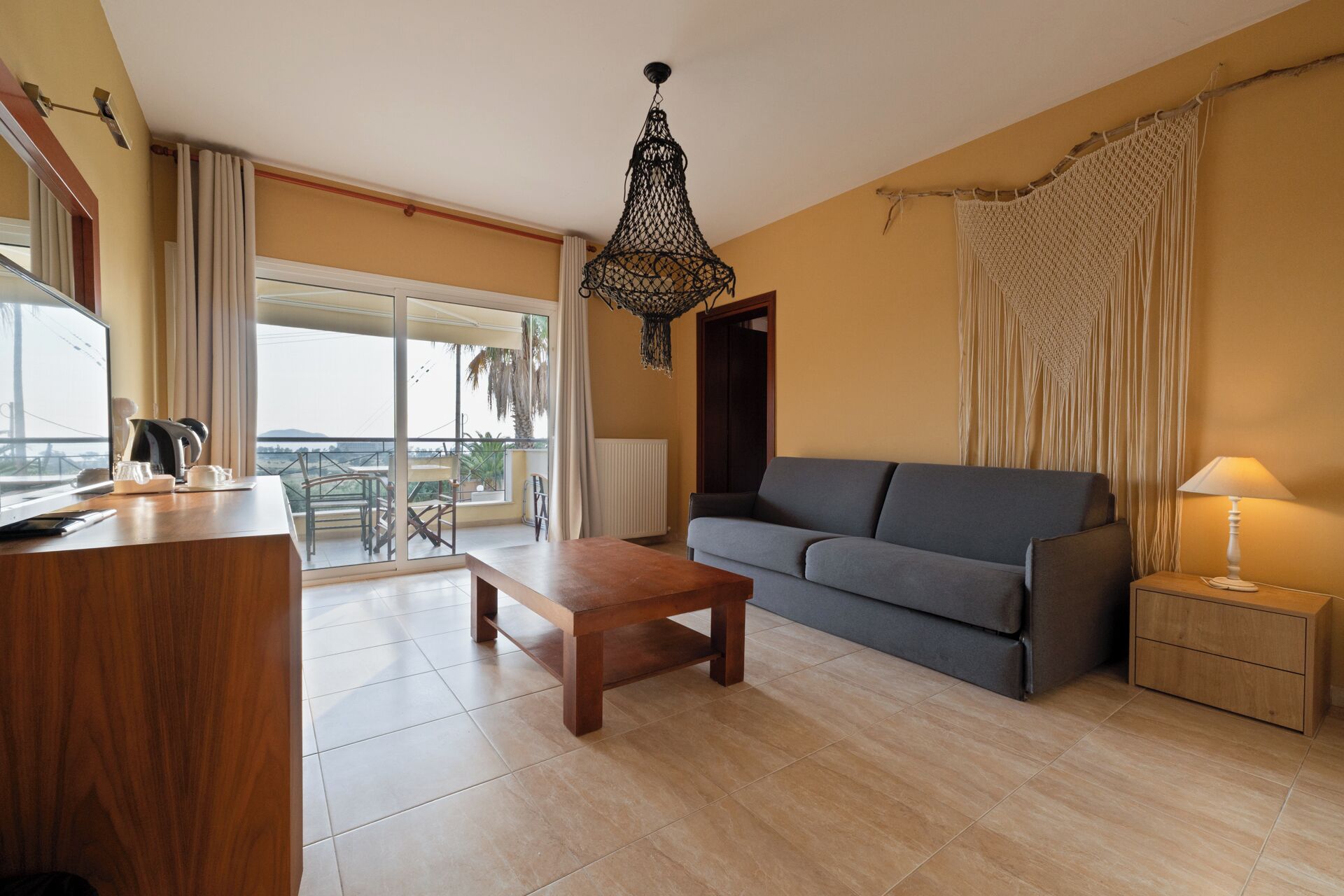A living room with a sofa, a wooden coffee table, a lamp, and a view through a large window.