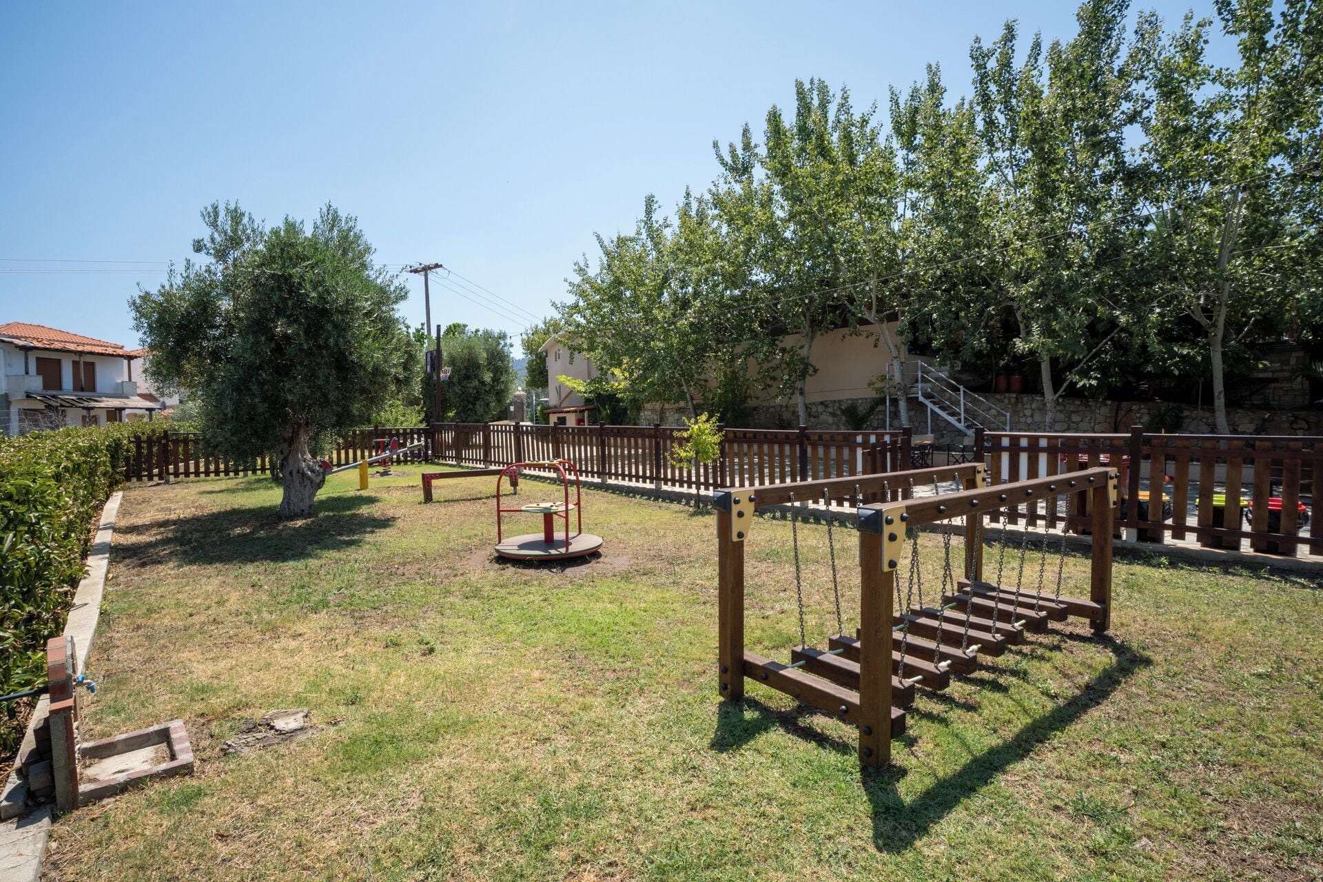 A playground with swings and a seesaw, surrounded by trees and a fence.