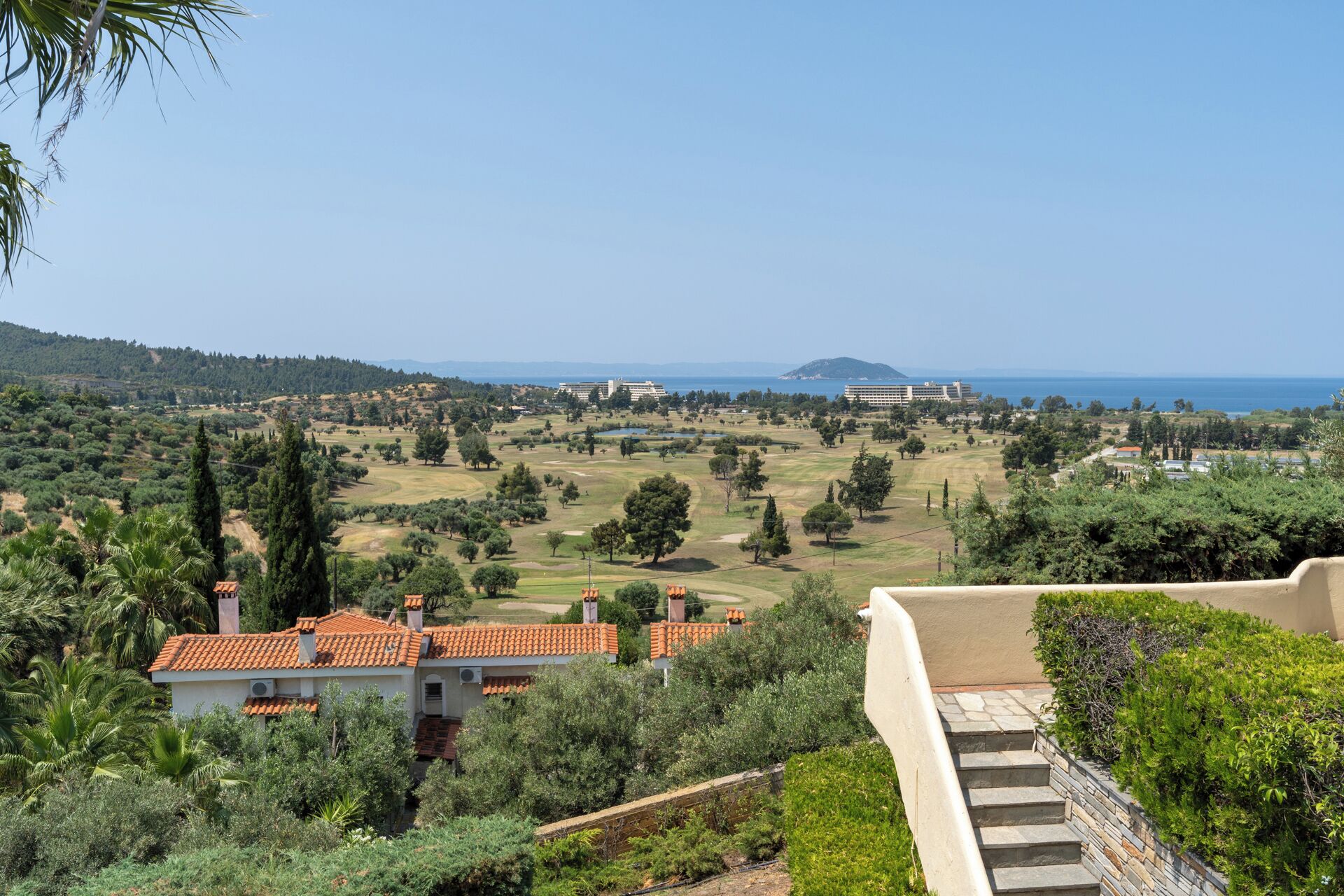 A coastal landscape with a golf course, buildings, and a clear view of the sea.