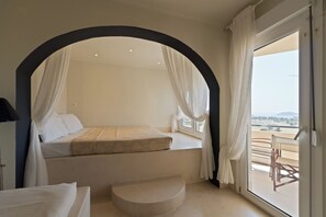 Un dormitorio con cama bajo dosel, una pequeña zona de estar y un balcón con vistas.