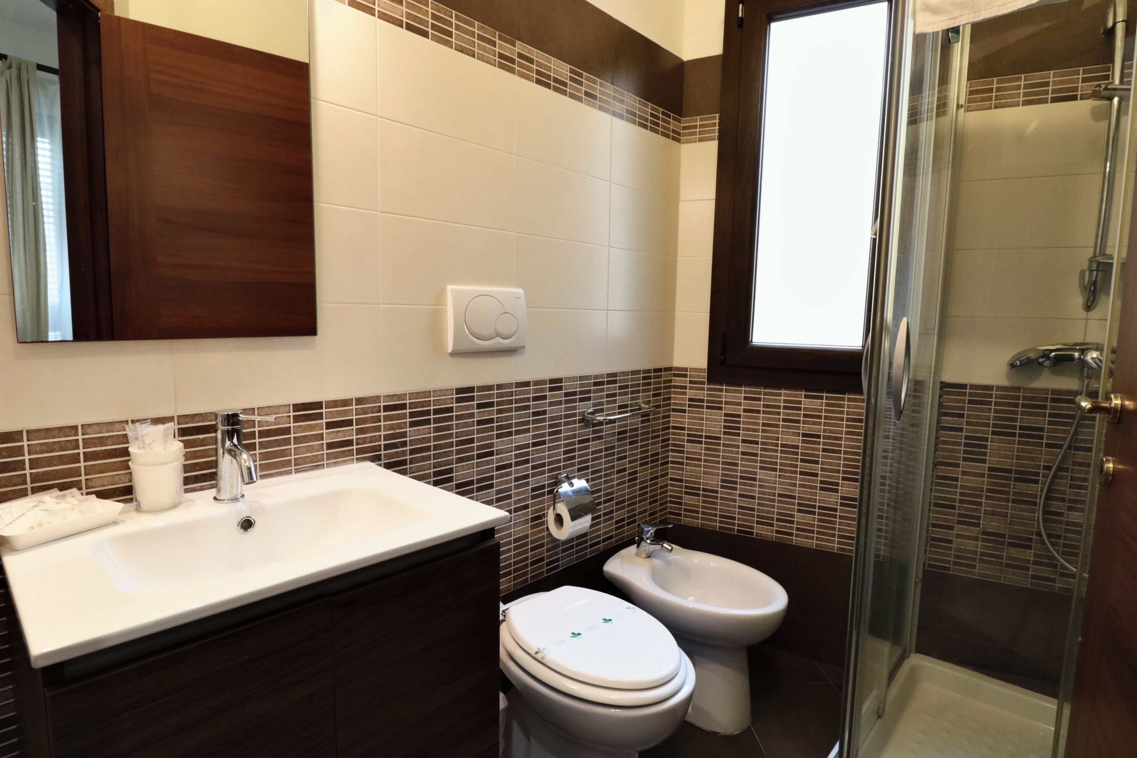 A bathroom with a sink, two toilets, a bidet, and a glass-enclosed shower.