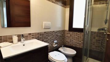 A bathroom with a sink, two toilets, a bidet, and a glass-enclosed shower.