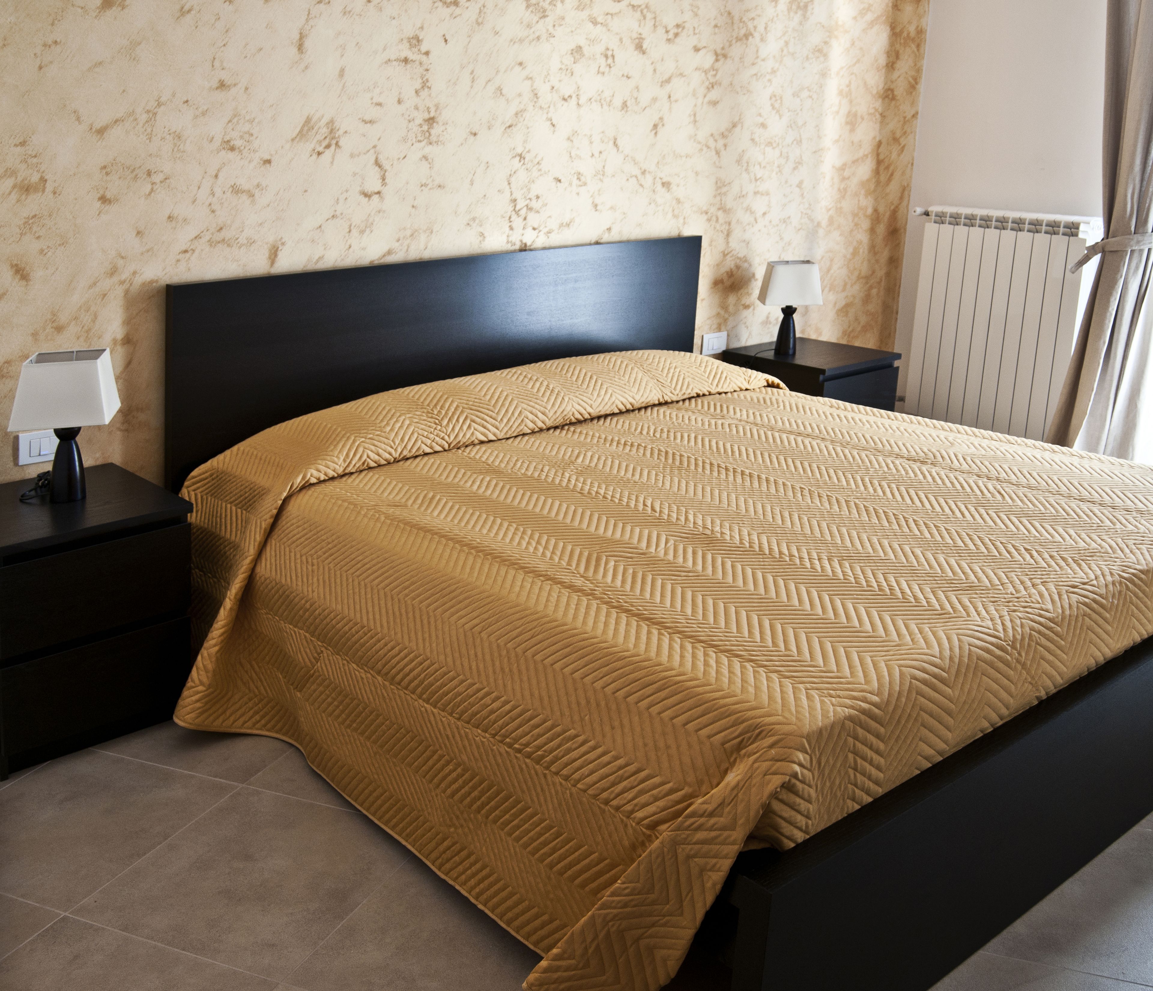 A bedroom with a bed, nightstands, a lamp, and a radiator.