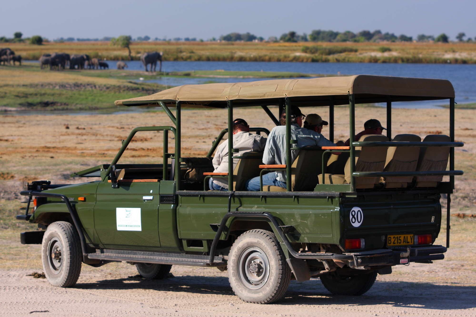 A safari vehicle with a roof, passengers, and a wildlife reserve in the background.