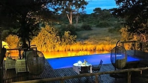 Une terrasse extérieure avec une piscine, entourée de végétation naturelle et dotée de rampes en bois.