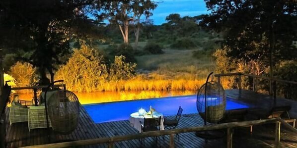 An outdoor deck with a pool, surrounded by natural vegetation and wooden railings.