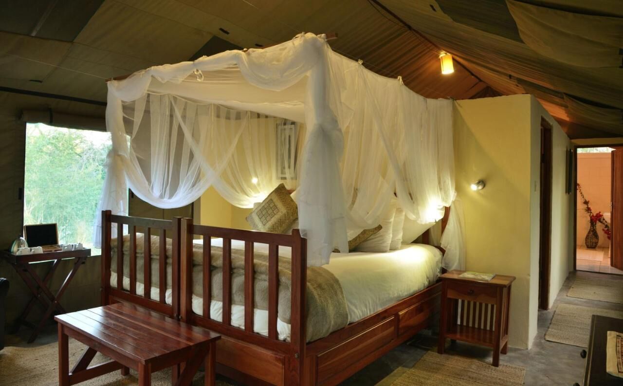 A four-poster bed with a canopy, wooden headboard, bedside tables, and a view of greenery outside.