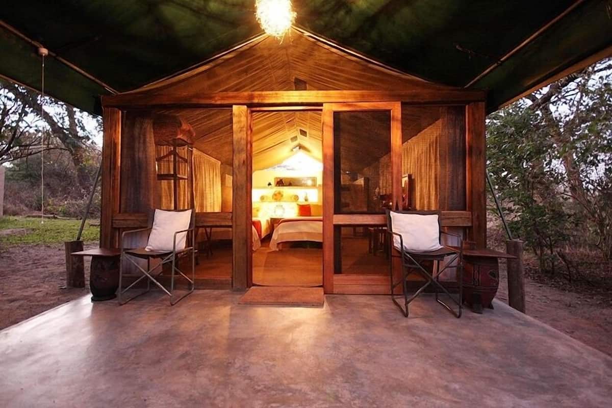 Una cabaña de madera rústica con un interior acogedor, que incluye dos sillones plegables y una cama con mesita de noche.
