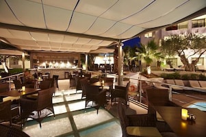 Un área de comedor al aire libre con mobiliario de mimbre, piscina y zona de bar.