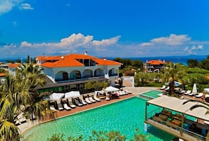 A resort with a pool, lounge chairs, and a building with a red roof. - Flegra Palace (Kassandra)