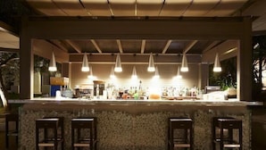 An outdoor bar area with a stone countertop, multiple hanging pendant lights, and wooden bar stools. - Flegra Palace (Kassandra)