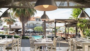 An outdoor dining area with tables and chairs, a pool, and a view of a building in the background. - Flegra Palace (Kassandra)