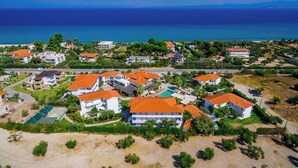 An aerial view of a coastal residential area with houses featuring red-tiled roofs, surrounded by greenery and a clear view of the ocean. - Flegra Palace (Kassandra)