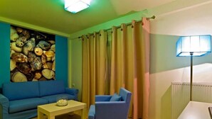 A living room with a blue sofa, a blue armchair, a wooden coffee table, and a wall decorated with seashells. - Flegra Palace (Kassandra)