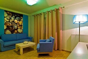 A living room with a blue sofa, a blue armchair, a wooden coffee table, and a wall decorated with seashells. - Flegra Palace (Kassandra)