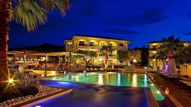 A hotel with a large outdoor swimming pool, multiple lounge areas, and a well-lit building facade. - Flegra Palace (Kassandra)