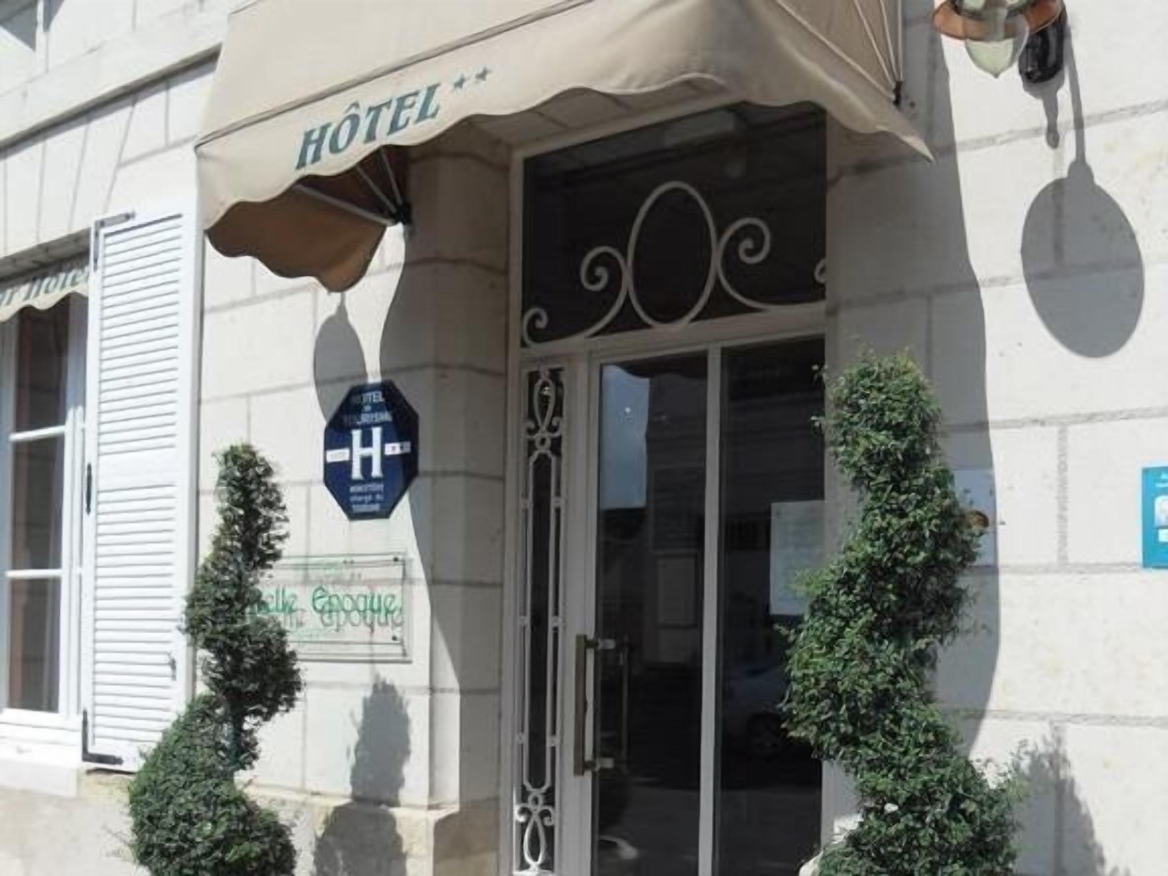 L’entrée d’un hôtel, avec une enseigne indiquant « Hôtel » et un panneau bleu portant un « H » blanc, qui signale la présence de l’hôtel.