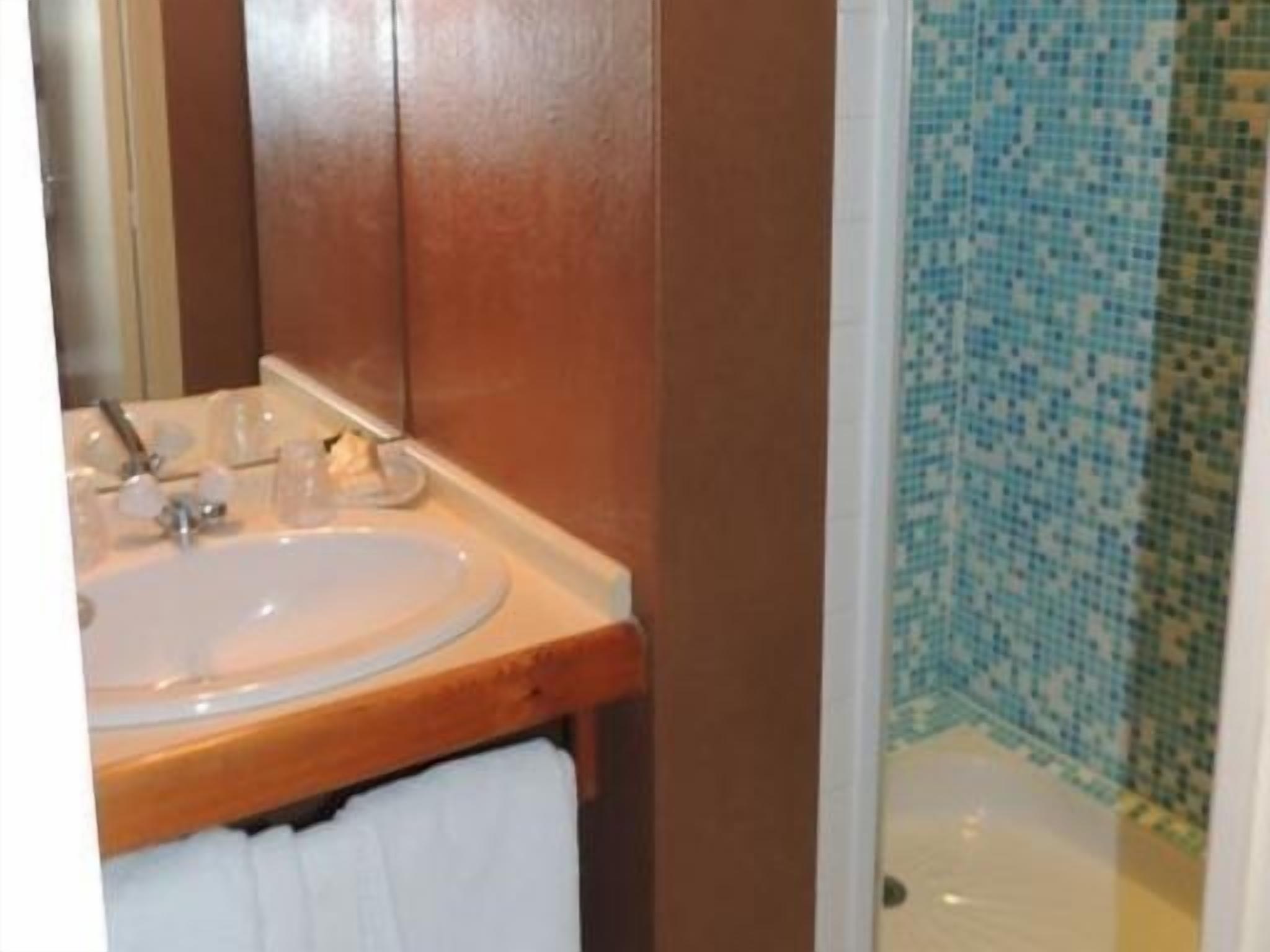 A bathroom with a sink, mirror, and shower area.