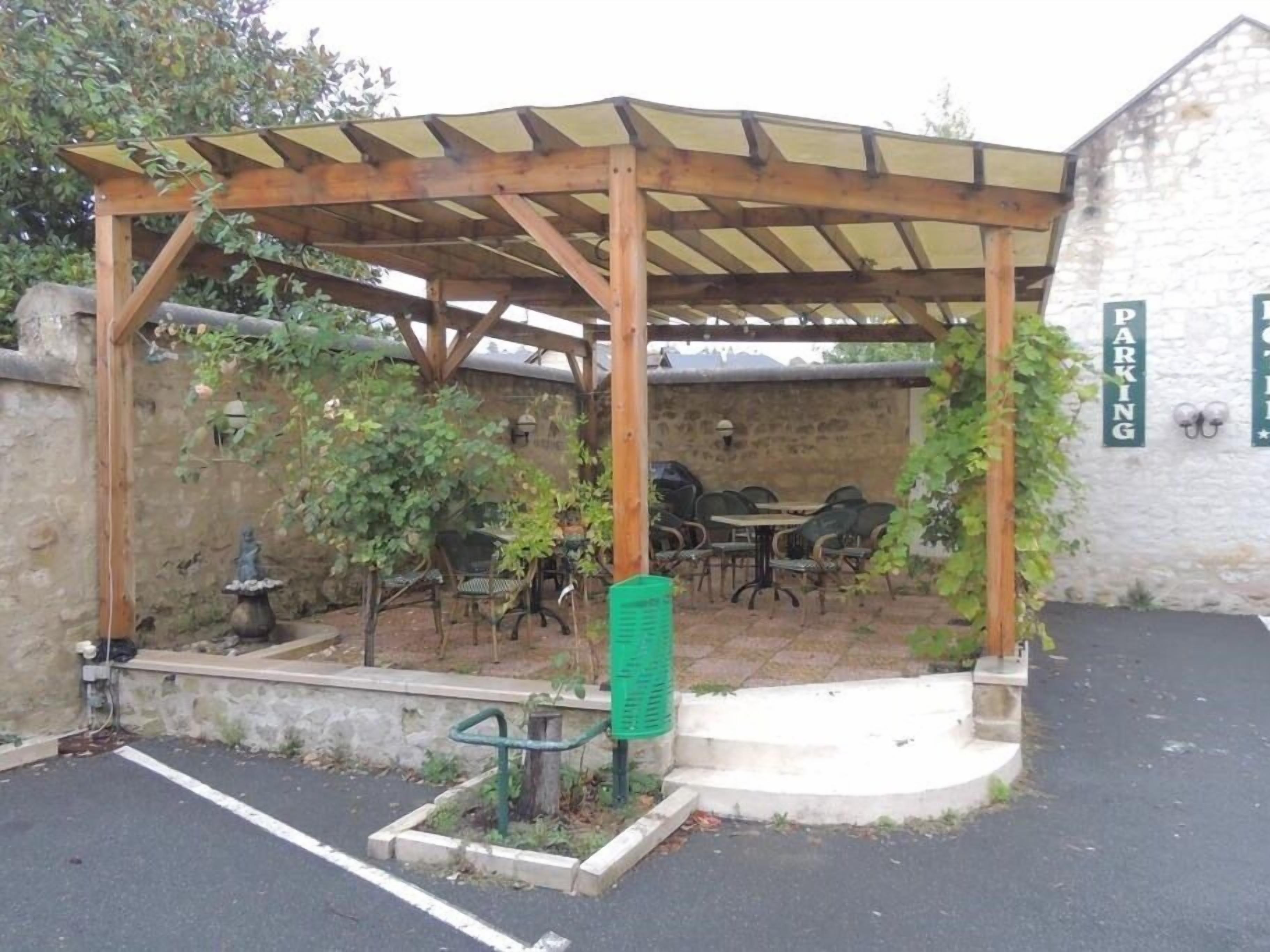 A covered outdoor seating area with tables and chairs, a stone wall, and a parking sign.
