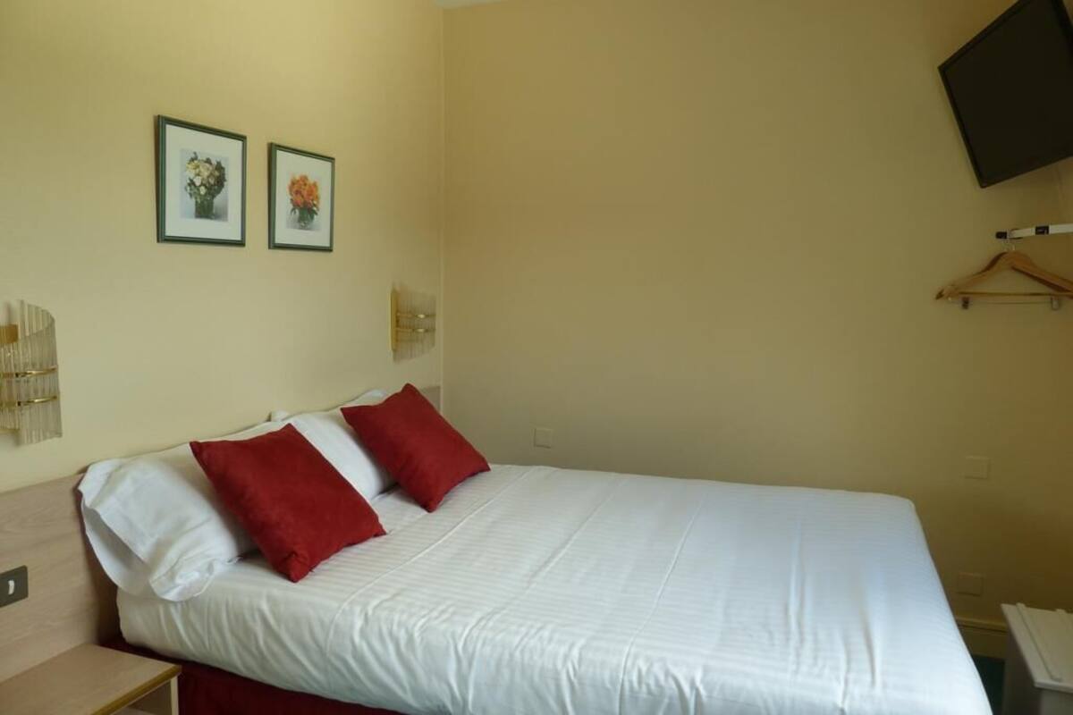 A single bed with white and red bedding, a wall-mounted TV, and two framed pictures on the wall.