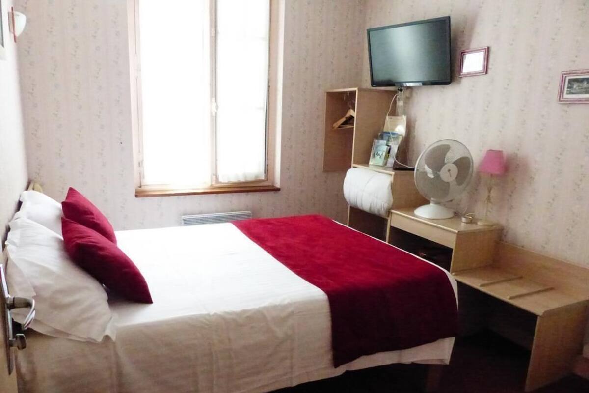 A hotel room with a bed, a TV, a desk with a fan, and a window.