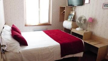 A hotel room with a bed, a TV, a desk with a fan, and a window.