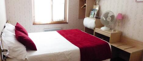 Een hotelkamer met een bed, een televisie, een bureau met een ventilator en een raam.