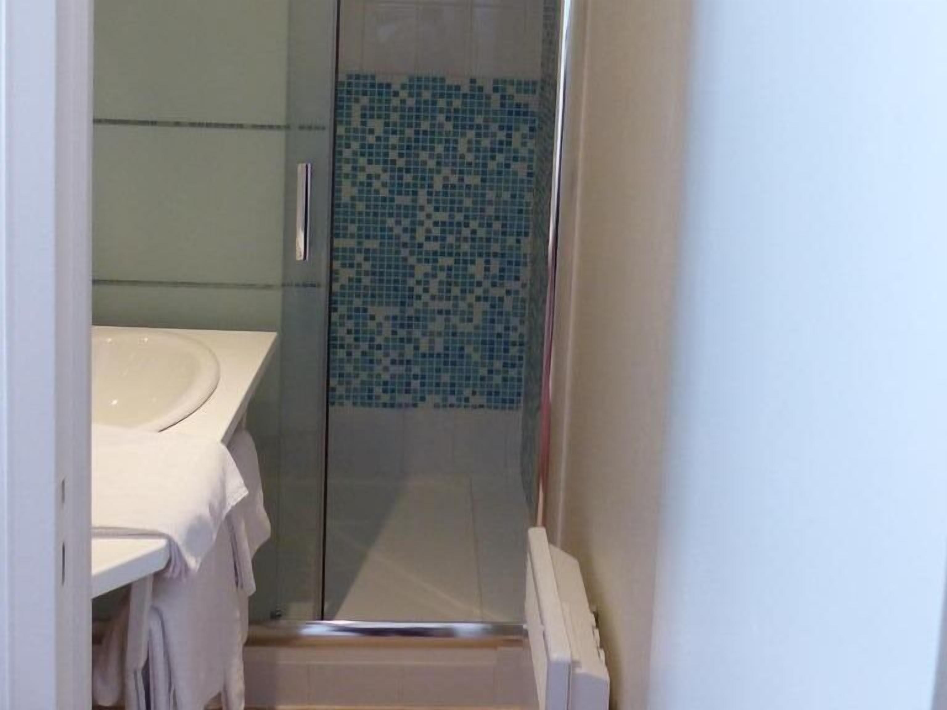 Un baño con cabina de ducha de vidrio, un lavabo blanco y un muro de ducha con azulejos.