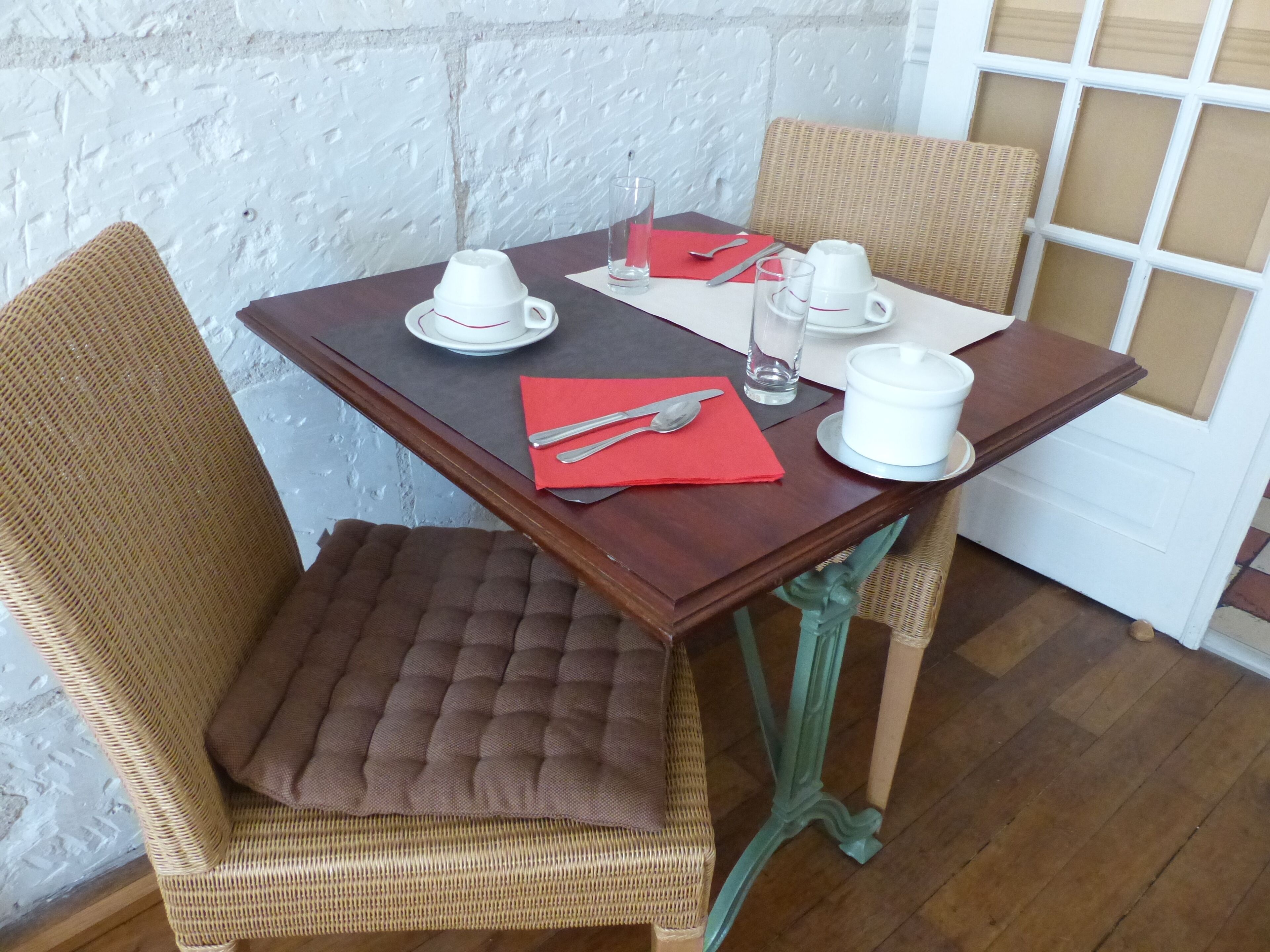 A dining table with white cups, a red napkin, and cutlery.