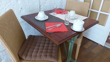 Una mesa de comedor con tazas blancas, un mantel individual rojo y cubiertos.