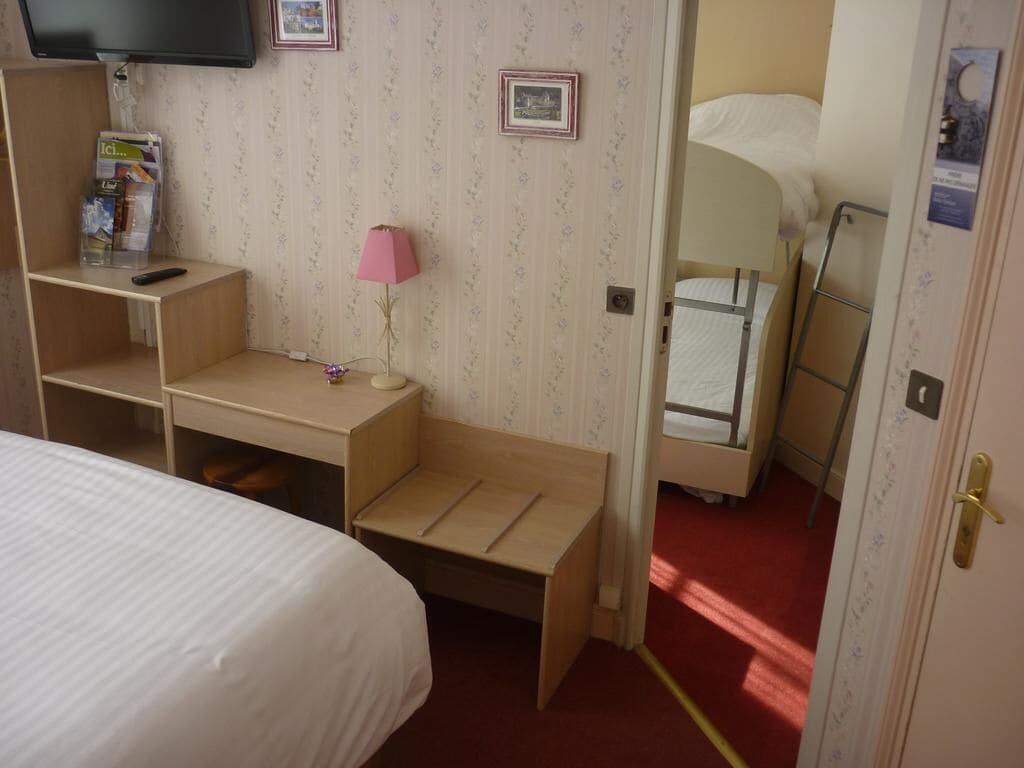 A bedroom with a bed, a desk with a lamp, a TV mounted on the wall, and a bunk bed.