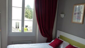 A hotel room with a bed, a window with curtains, a wall-mounted light, and a framed picture. - Hôtel Belle Epoque (Chinon)