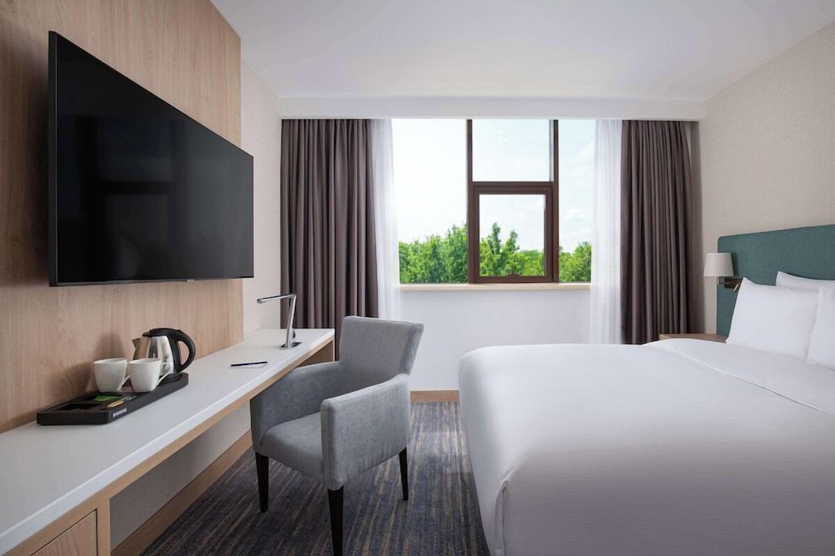 A hotel room with a bed, a desk, a chair, a flat-screen TV, and a window with curtains.