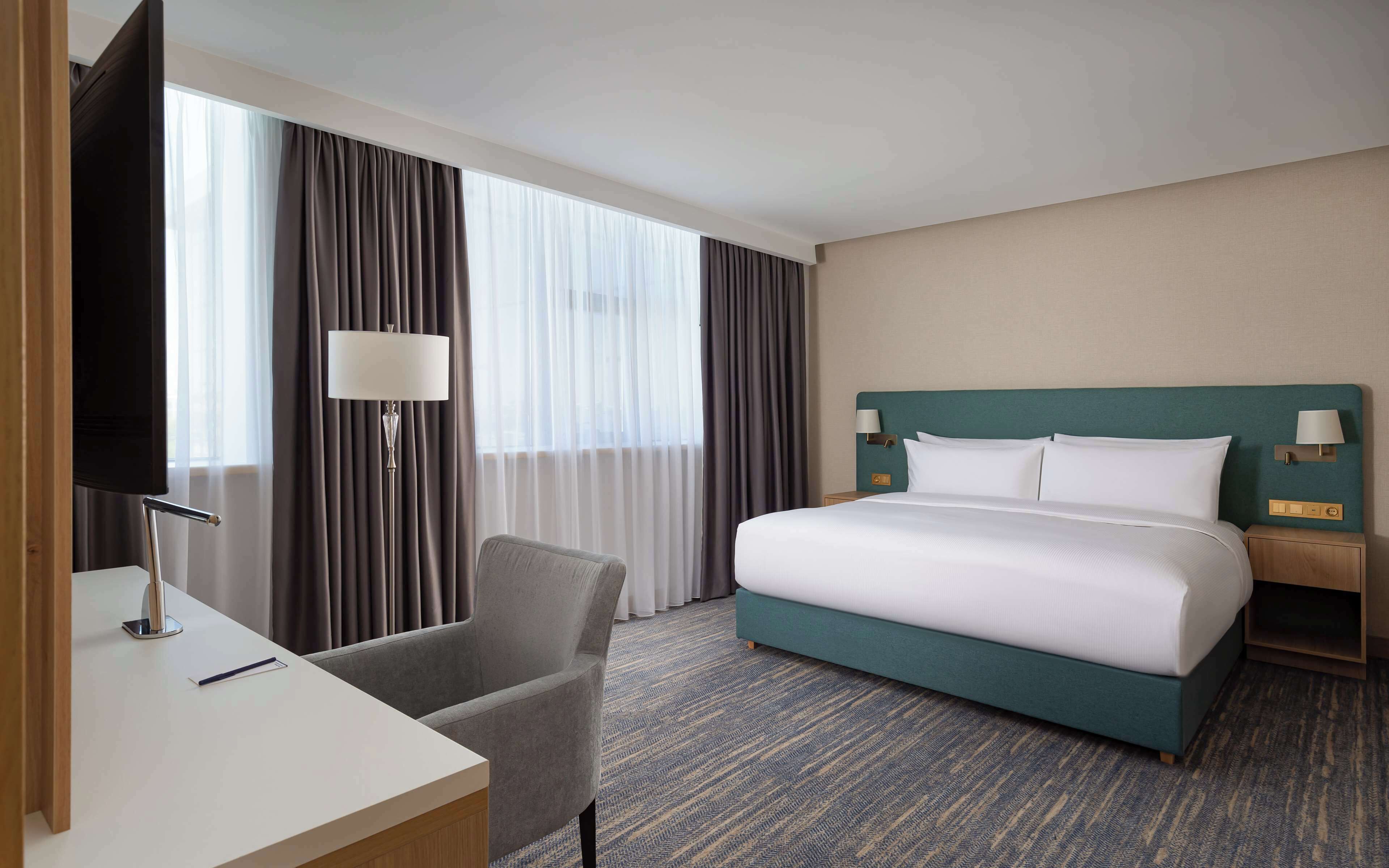 Una habitación de hotel con una cama grande, un escritorio con una silla, un televisor y una lámpara.