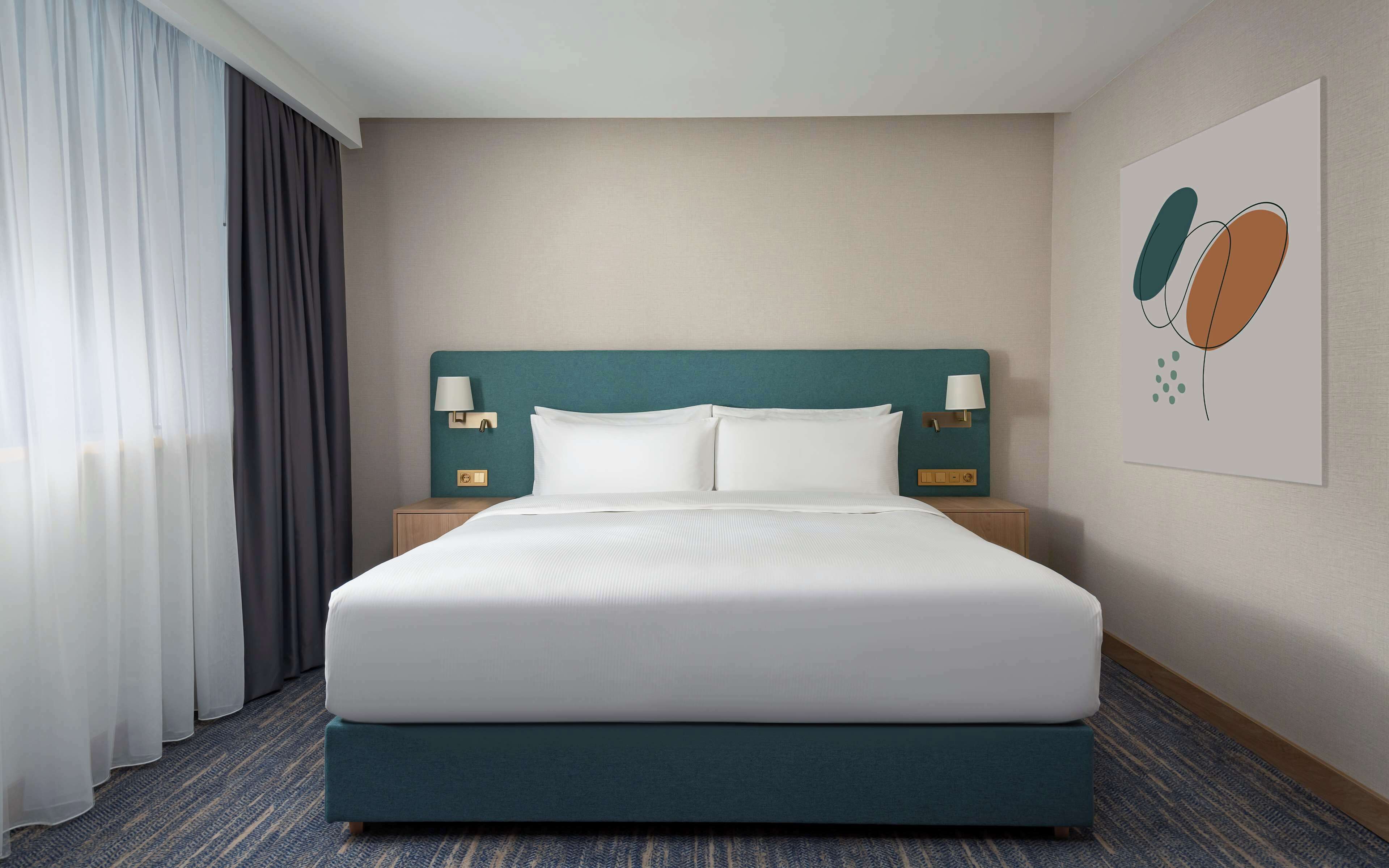 Une chambre d’hôtel avec un grand lit, deux tables de chevet avec des lampes, une tête de lit et un mur orné d’un tableau encadré.