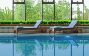 Un espace piscine avec deux chaises longues en bois et une vue sur les arbres à travers de grandes fenêtres.