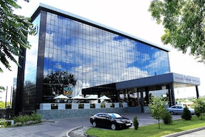 Un bâtiment moderne doté d’une façade en verre, d’un espace d’entrée abrité et d’un parking où sont garées des voitures.